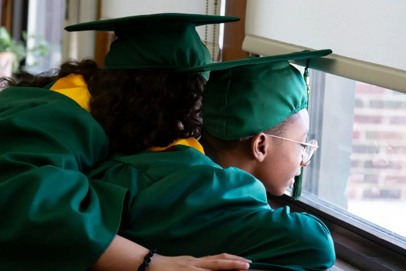 Nativity Preparatory Academy students in academic regalia looking out a window together